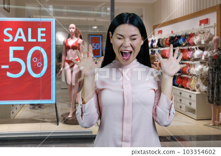 Young hysterical asian woman screaming out loud. Lingerie boutique with half discount in the background. Young hysterical asian woman screaming out loud. Lingerie boutique with half discount in the background. 103354602