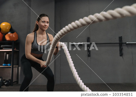 Crossfit female athlete exercising with battle ropes at gym Crossfit female athlete exercising with battle ropes at gym 103354851