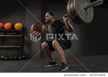 Muscular crossfiter doing squats exercise with barbell 103354889