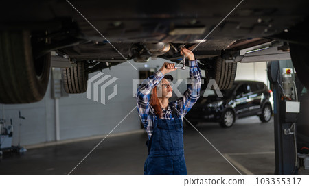 Female mechanic unscrew the nuts on the bottom of the car that is on the lift. A girl at a man's work. Female mechanic unscrew the nuts on the bottom of the car that is on the lift. A girl at a man's work. 103355317