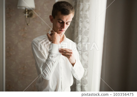 Grooms morning preparation. Handsome man getting dressed and preparing for the wedding Grooms morning preparation. Handsome man getting dressed and preparing for the wedding 103356475