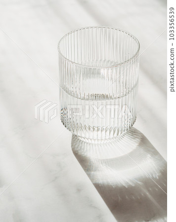 Glass with clean clear water and shadows stands on a white table 103356539