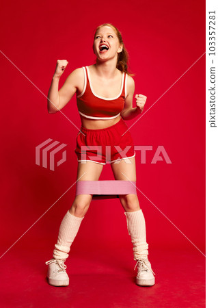 Happy sporty girl wearing sportswear and doing exercise with rubber bands for sport over red background. Gluteal muscles workout 103357281