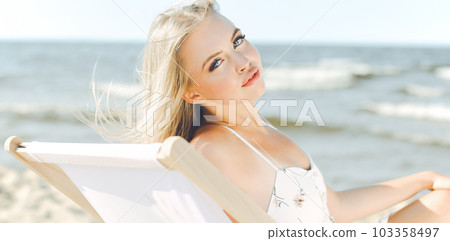 Happy blonde woman relaxing on a wooden deck chair at the ocean beach Happy blonde woman relaxing on a wooden deck chair at the ocean beach 103358497