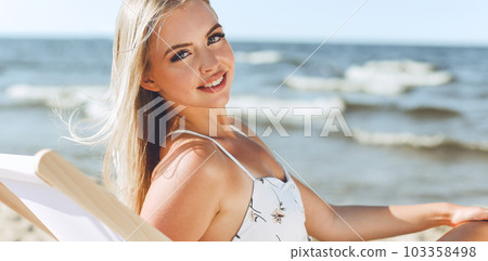Happy blonde woman relaxing on a wooden deck chair at the ocean beach Happy blonde woman relaxing on a wooden deck chair at the ocean beach 103358498