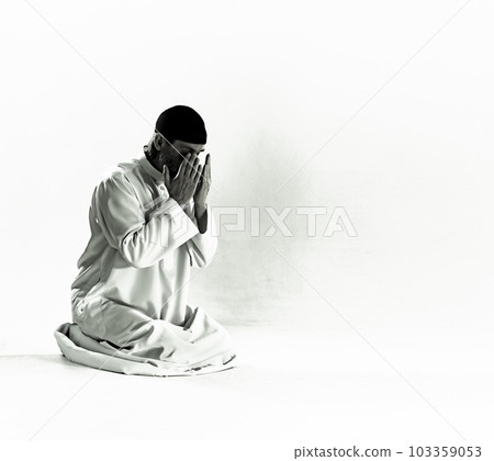 Islam religious concept.Muslim man in traditional clothing kneels on prayer mat, holds palms in front of face and performs Salah, ritual prayer of Islam. devotion, piety, and spiritual aspect of 103359053