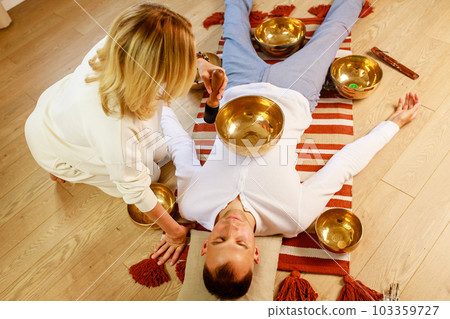 Woman playing on a tibetian singing bowl maling massage meditation for a man Woman playing on a tibetian singing bowl maling massage meditation for a man 103359727