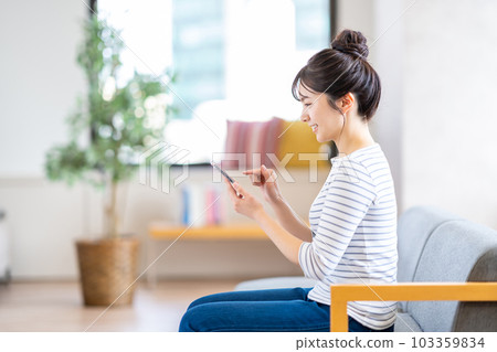 一名年輕女子在客廳裡使用智能手機。 103359834