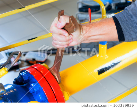 The worker tightens the nut of the gas equipment with an adjustable wrench. hands close up The worker tightens the nut of the gas equipment with an adjustable wrench. hands close up 103359939