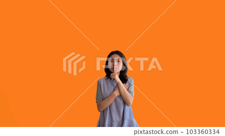Asian woman doing silent gesture with finger, Noiseless symbol, Noisy mall, Hide a secret, Do not speak. shut your mouth, Noiseless signal transmission, Isolated on orange background. Asian woman doing silent gesture with finger, Noiseless symbol, Noisy mall, Hide a secret, Do not speak. shut your mouth, Noiseless signal transmission, Isolated on orange background. 103360334