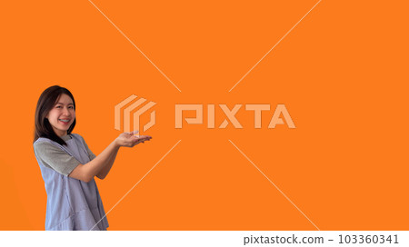 Asian woman with holding copyspace imaginary on the palm to insert an ad, Showing copyspace pointing, Showing her hand to present something on orange background. 103360341