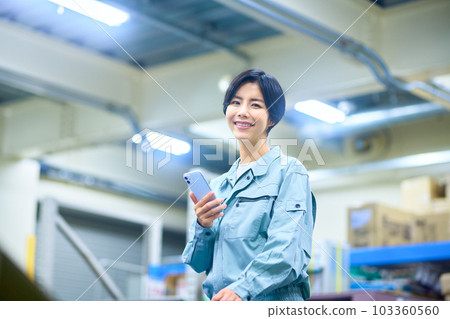 Female businessman in work clothes operating a smartphone in a warehouse Female businessman in work clothes operating a smartphone in a warehouse 103360560