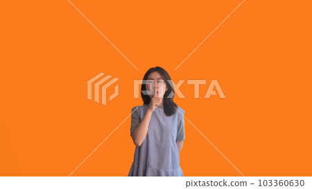 Asian woman doing silent gesture with finger, Noiseless symbol, Noisy mall, Hide a secret, Do not speak. shut your mouth, Noiseless signal transmission, Isolated on orange background. Asian woman doing silent gesture with finger, Noiseless symbol, Noisy mall, Hide a secret, Do not speak. shut your mouth, Noiseless signal transmission, Isolated on orange background. 103360630