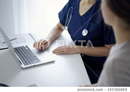 Doctor and patient sitting at the desk in clinic office. The focus is on unknown female physician's hands using a laptop computer, close up. Medicine concept 103360869