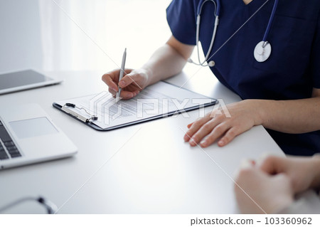 Doctor and patient sitting at the table in clinic while discussing something. The focus is on female physician's hands, close up. Medicine concept 103360962
