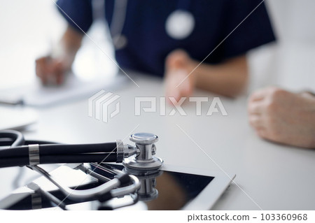 Stethoscope lying on the tablet computer in front of a doctor and patient at the background. Medicine, healthcare concept 103360968