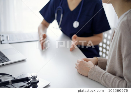 Doctor and patient sitting at the table in clinic while discussing something. The focus is on female patient's hands, close up. Medicine concept Doctor and patient sitting at the table in clinic while discussing something. The focus is on female patient's hands, close up. Medicine concept 103360976