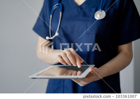 Doctor woman using tablet computer while standing near panorama window in clinic, close up. Physician or surgeon at work. Medicine concept 103361007