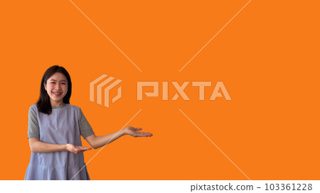 Asian woman with holding copyspace imaginary on the palm to insert an ad, Showing copyspace pointing, Showing her hand to present something on orange background. 103361228