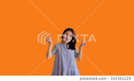 Young Asian woman making two thumbs up gesture showing joy and fun, Symbol of good friendship, Popular photo poses, Make a v-shaped finger, Orange background. Young Asian woman making two thumbs up gesture showing joy and fun, Symbol of good friendship, Popular photo poses, Make a v-shaped finger, Orange background. 103361229