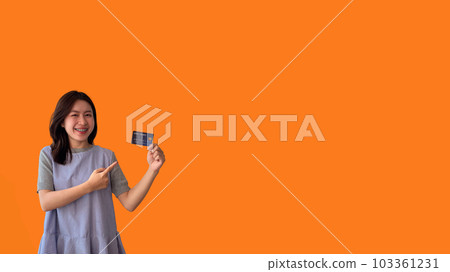 Asian woman holding credit card and thumbs up on orange background, Suggest or demonstrate the use of credit cards instead of cash, Payment, Finance, Transact or spend online. 103361231