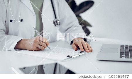 Unknown doctor woman sitting and writing notes at the desk in clinic or hospital office, close up. Medicine concept 103361477