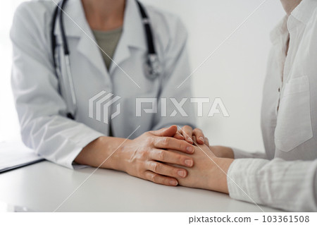 Doctor and patient sitting at the desk in clinic office. The focus is on female physician's hands reassuring woman, close up. Perfect medical service, empathy, and medicine concept Doctor and patient sitting at the desk in clinic office. The focus is on female physician's hands reassuring woman, close up. Perfect medical service, empathy, and medicine concept 103361508