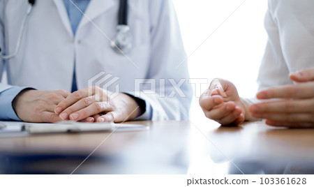 Doctor and patient discussing something while sitting near each other at the wooden desk in clinic. Medicine concept 103361628