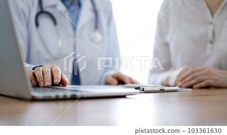 Doctor and patient discussing something while using laptop computer and sitting near each other at the wooden desk in clinic. Medicine concept 103361630
