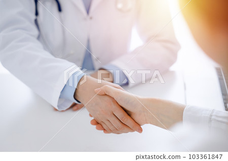 Doctor and patient shaking hands while sitting opposite of each other at the table in clinic, just hands close up. Medicine concept Doctor and patient shaking hands while sitting opposite of each other at the table in clinic, just hands close up. Medicine concept 103361847
