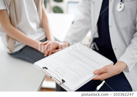 Doctor and child patient. The physician is holding clipboard and reassuring a boy. The concept of ideal health in medicine Doctor and child patient. The physician is holding clipboard and reassuring a boy. The concept of ideal health in medicine 103362247