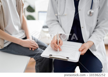 Doctor and child patient. The physician is holding clipboard and writing in medical record form near a boy. The concept of ideal health in medicine 103362252