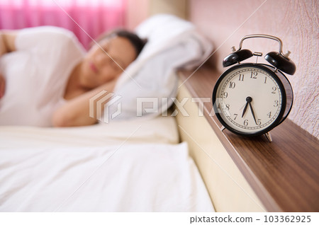 Selective focus on black alarm clock on blur background of pregnant woman, expectant mother sleeping, napping at daytime, renewing her energy, taking care of the health of her future baby. Pregnancy 103362925