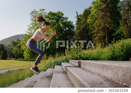Sporty woman doing jumping squats exercise on stairs in city park. Sporty woman doing jumping squats exercise on stairs in city park. 103363109