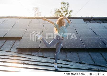 Portrait of young excited woman on roof with solar panels. 103363137