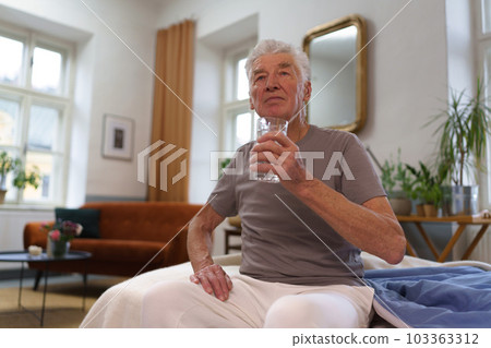 Portrait of senior man drinking water after taking pills, medications. 103363312