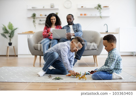 Kids playing with toys while parents using laptop in kitchen 103363403