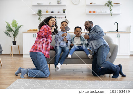 Parents and sons singing with kitchen utensils at home Parents and sons singing with kitchen utensils at home 103363489