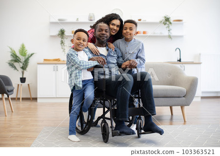 Woman cuddling children and husband with disability at home 103363521