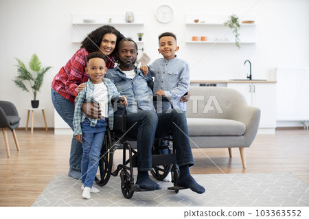 Man in wheelchair hugging wife and kids in living room 103363552