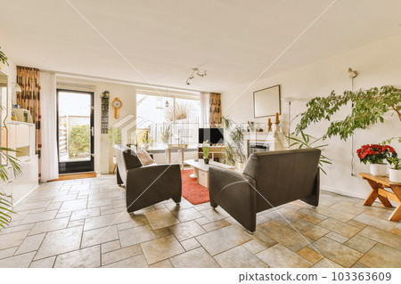 a living room with couches, chairs and plants in the middle of the room on the right is an open door that leads 103363609