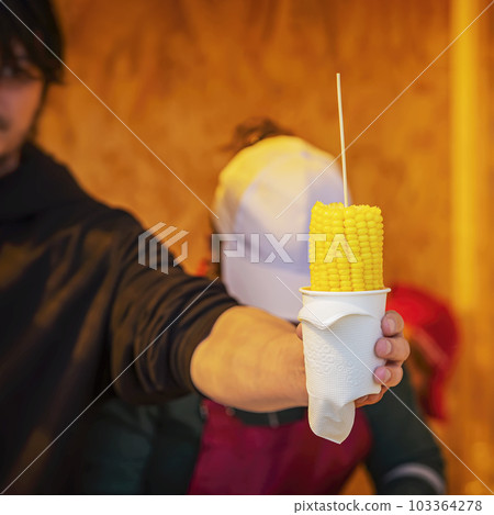 Close-up hands of male street vendor with sweet corn on stick. Street food, summer grill concept 103364278