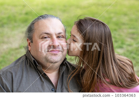 Daughter kisses her father in the park. Father's Day. Happy daughter kisses her father. Close-up. Copyspace. Daughter kisses her father in the park. Father's Day. Happy daughter kisses her father. Close-up. Copyspace. 103364363