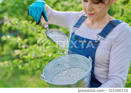 Close-up of female gardener's hand with iron bucket of granular fertilizer Close-up of female gardener's hand with iron bucket of granular fertilizer 103366338