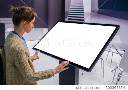 Woman using interactive empty white touchscreen display kiosk at exhibition 103367854