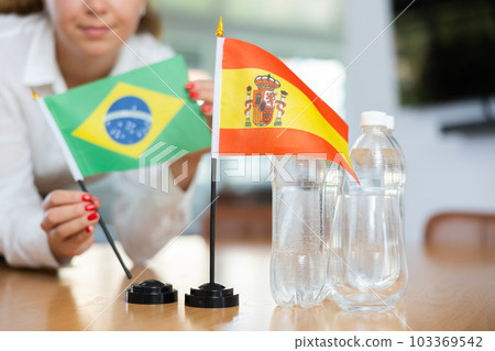 Little flag of Spain on table and flag of Brazil put next to it by young woman 103369542