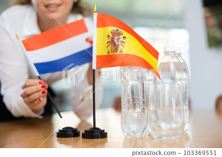 Little flag of Spain on table and flag of Netherlands put next to it by young woman 103369551