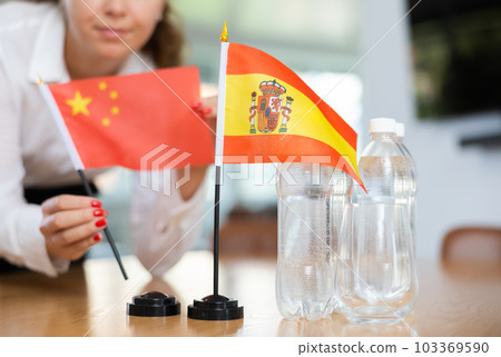 Little flag of Spain on table and flag of China put next to it by young woman 103369590