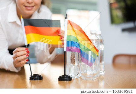 Unrecognizable girl sets midget flags of LGBT and Germany before international negotiations 103369591