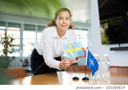 Employee of delegation prepares negotiating table - sets up flag of NATO (OTAN) and Sweden Employee of delegation prepares negotiating table - sets up flag of NATO (OTAN) and Sweden 103369814